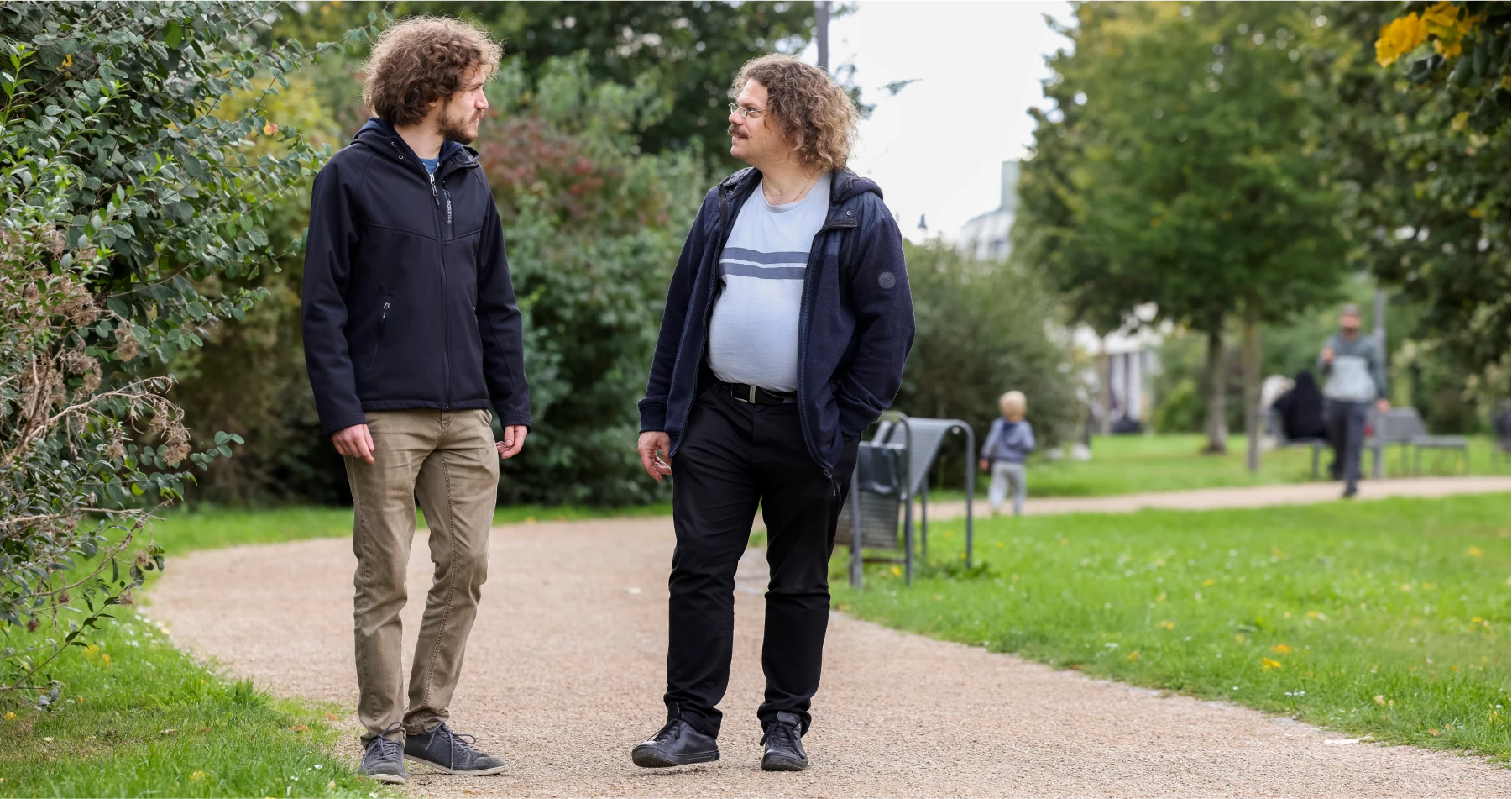 headerbild_inklusion_im_stadtteil Zwei Männer unterhalten sich beim Spazierengehen im Park.