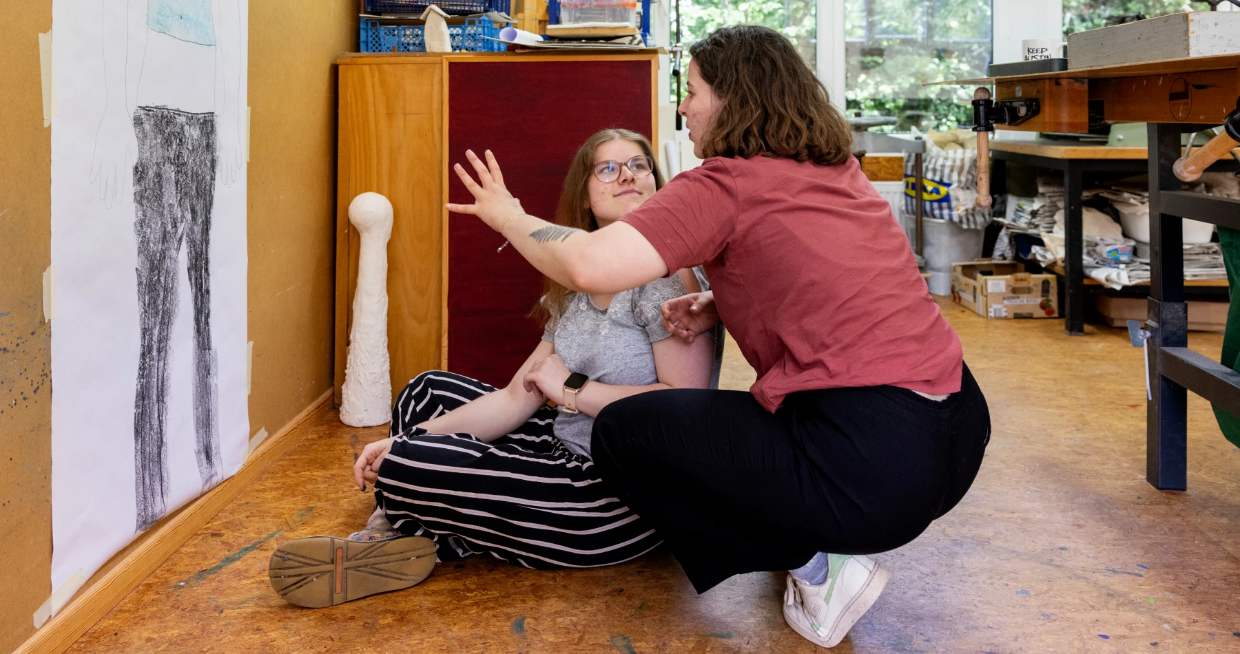 Zwei Frauen besprechen ein gemaltes Bild, das an der Wand hängt.