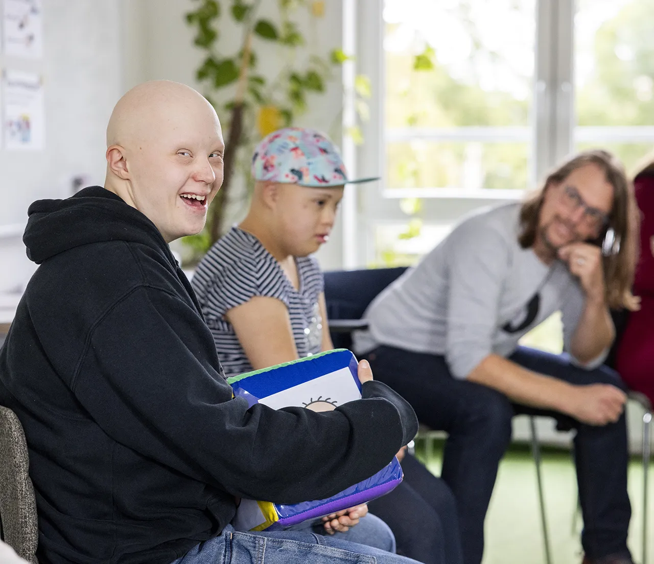 Ein Man in weißem T-Shirt schneidet ein Holunderblüte ab, im Hintergrund schauen zwei Frauen zu.